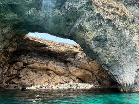A stunning view of a natural rock arch with swimmers enjoying the clear waters below, showcasing the beauty of coastal adventures.