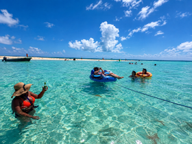 A vibrant group enjoys a fun day at the sandbar, swimming and relaxing in the crystal-clear waters with drinks in hand — the perfect tropical getaway.