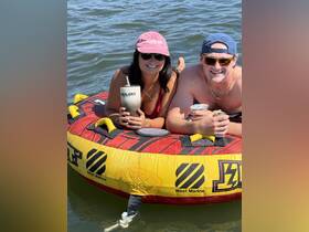 A couple enjoys a sunny day tubing on the water, sipping drinks and soaking up the summer vibes — perfect for a fun-filled day on the lake.