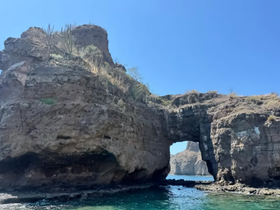 A stunning view of a natural rock formation arching over clear waters, showcasing the beauty of coastal landscapes — perfect for nature lovers and adventure seekers.