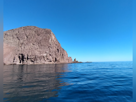 A stunning view of a rocky coastline under a clear blue sky, showcasing the serene beauty of the ocean — perfect for nature lovers and scenic boat trips.