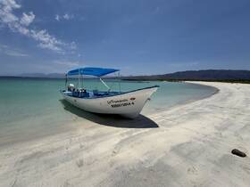 A picturesque view of a boat named 'La Trompudita' docked on a serene beach, surrounded by clear turquoise waters and a stunning mountainous backdrop.