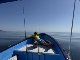A man relaxes on the bow of a fishing boat, enjoying a calm day on the ocean — perfect for fishing enthusiasts seeking tranquility on the water.