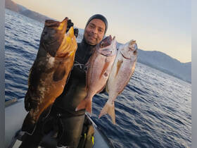 A proud fisherman displays his impressive catch of fish against a stunning ocean backdrop at sunset, showcasing the thrill of a successful fishing trip.