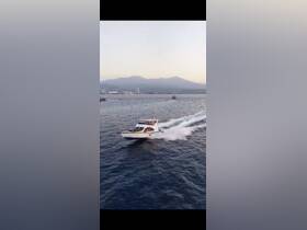 A stunning aerial view of a speedboat cruising through the water, showcasing its sleek design against a backdrop of mountains and coastline.