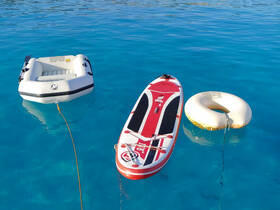 A vibrant scene showcasing a paddleboard, inflatable boat, and a floating ring in crystal-clear waters, perfect for a day of fun and relaxation on the water.