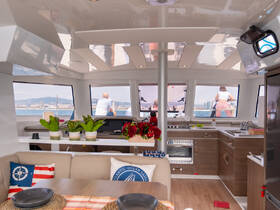 A stylish interior view of a catamaran's cabin, featuring a cozy seating area and a glimpse of guests enjoying the scenery outside.