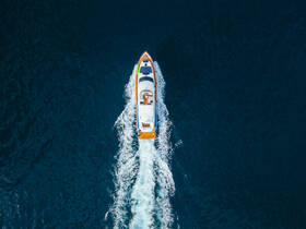 A stunning aerial view of a yacht cruising through deep blue waters, showcasing its sleek design and vibrant colors — perfect for luxury boating experiences.