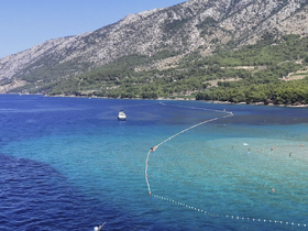A stunning view of a serene coastline with a boat anchored nearby, while people enjoy swimming in the clear turquoise waters — a perfect summer getaway.