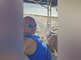 A man enjoys a relaxing moment on a boat, with a scenic view of the beach and water in the background — perfect for a day of leisure on the water.