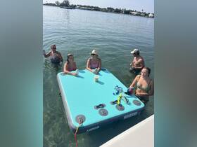 A lively group enjoys a day on a floating mat in clear waters, sipping cocktails and soaking up the sun — perfect for summer fun and relaxation.
