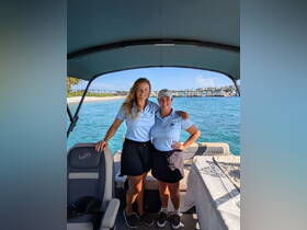 Two crew members pose together on a boat, ready to welcome guests for a day of fun on the water. Their smiles and the beautiful backdrop highlight the joy of boating adventures.