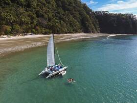 A vibrant scene featuring a catamaran anchored near a beautiful beach, with guests enjoying the water and swimming — perfect for a day of adventure and relaxation.