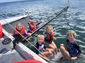 A joyful group of children enjoys a fun day on the water, playing and swimming off the side of a catamaran, showcasing the excitement of aquatic adventures.