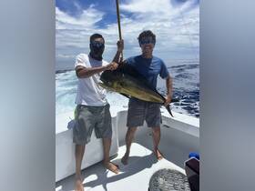 Two anglers proudly display their catch aboard a fishing boat, showcasing the thrill of deep-sea fishing in the open ocean.