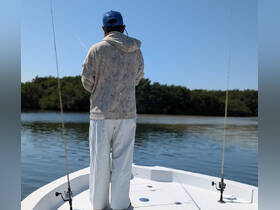 A fisherman casts his line from the deck of a boat, surrounded by serene waters and lush mangroves — a perfect day for fishing adventures.