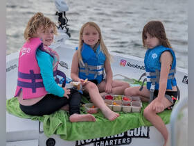 Three children enjoy snacks on a boat, showcasing a fun and safe boating experience with life jackets and a variety of treats.