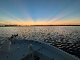 A serene sunset view from the bow of a boat, showcasing the tranquil waters and vibrant sky — perfect for evening cruises.