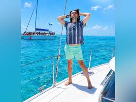A man enjoys the sun while sailing on a catamaran, showcasing the vibrant blue ocean and a lively atmosphere in the background.