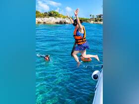 A woman joyfully jumps into the clear turquoise waters, while another snorkeler enjoys the vibrant underwater scenery — perfect for adventurous water activities.