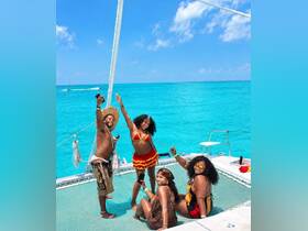 A lively group of friends enjoys a fun day on a catamaran, celebrating under the sun with stunning turquoise waters as their backdrop.