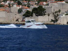 A speedboat named 'MY DREAM' glides through the vibrant blue waters near a historic coastline, showcasing the beauty of the surrounding architecture and landscape.