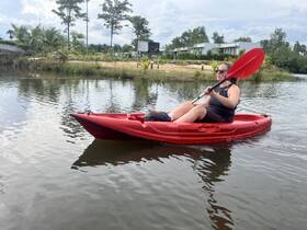 A woman enjoys kayaking in a vibrant red kayak, navigating through calm waters surrounded by lush greenery — a perfect adventure for water enthusiasts.