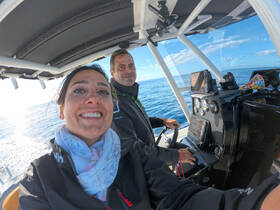 A cheerful selfie of two individuals at the helm of a boat, showcasing the modern console and the serene ocean backdrop — perfect for capturing the excitement of a day on the water.