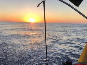A stunning sunset over the open ocean, viewed from the deck of a boat, creating a serene and picturesque maritime scene.