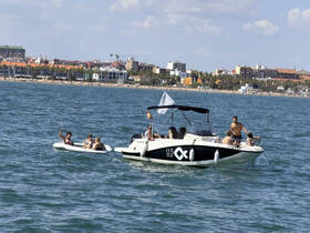 A lively group enjoys a day on the water, with some relaxing on a boat and others on a paddleboard, capturing the essence of summer fun at the beach.