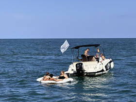A lively group enjoys a day on the water, relaxing on a floating mat while a boat is anchored nearby — perfect for summer fun and water activities.