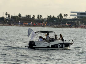 A lively group enjoys a day on the water aboard a sleek boat, with a vibrant beach scene in the background, perfect for summer outings and celebrations.