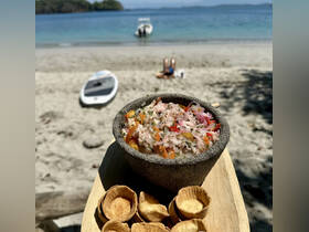 A delicious seafood dish served with crispy snacks, perfect for enjoying on the beach while taking in the scenic views of the water and nearby boat.