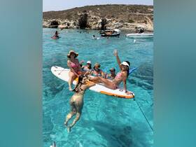 A lively group enjoys a fun day on the water, paddleboarding and celebrating with cocktails in crystal-clear waters — perfect for summer adventures.