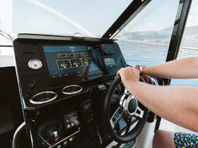 A close-up view of a boat's helm with a person steering, showcasing modern navigation equipment and controls — perfect for those looking to explore the open waters.