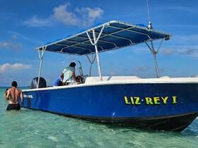 Two individuals interact near the boat 'LIZ-REY I' in shallow turquoise waters, capturing the essence of a fun day at the beach.