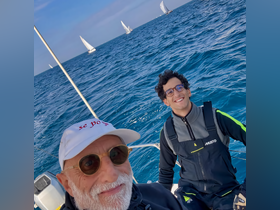 Two friends enjoy a sailing adventure on the ocean, capturing a joyful moment with the backdrop of other sailboats in the distance.