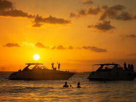 A vibrant sunset scene captures groups of people enjoying a boating experience, with silhouettes against the glowing horizon — perfect for memorable celebrations on the water.