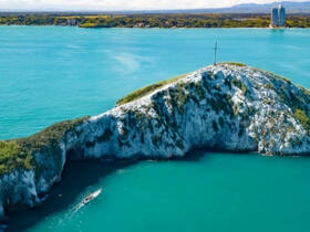 A stunning aerial view of a rocky island with a cross, surrounded by vibrant turquoise waters — a picturesque destination perfect for boating adventures.