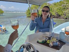 Guests toast with cocktails on a boat, enjoying a delightful spread of snacks while surrounded by beautiful waters — a perfect setting for relaxation and celebration.