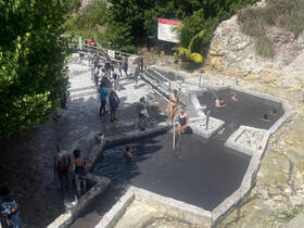 Visitors enjoy a relaxing day at a natural mud bath, surrounded by lush greenery — a perfect spot for rejuvenation and fun in the sun.