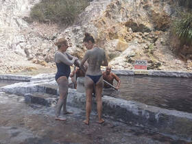 A group of friends enjoys a mud bath experience in a natural pool, surrounded by stunning rocky scenery — perfect for relaxation and rejuvenation.