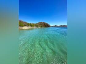 A stunning view of a tranquil beach with crystal-clear turquoise waters and lush greenery, perfect for a relaxing getaway or eco-tour in nature.