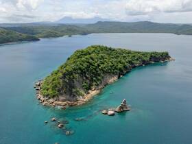 A stunning aerial view of a lush island surrounded by clear turquoise waters, showcasing the natural beauty of the coastline — perfect for eco tours and island hopping adventures.