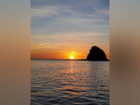 A stunning sunset casts vibrant colors over the tranquil waters, with a rocky coastline silhouetted against the sky — a perfect backdrop for evening boat trips.