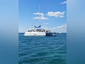 A lively catamaran cruising through clear waters, filled with guests enjoying the sun and sea — perfect for group outings and adventures.