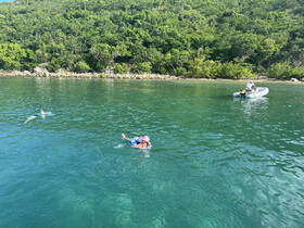 A group enjoys swimming in crystal-clear waters, with a scenic backdrop of lush greenery — perfect for a day of snorkeling and aquatic adventures.