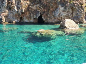 A stunning view of a rocky coastline with a cave entrance, surrounded by crystal-clear turquoise waters — a perfect destination for exploration and adventure.
