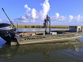 A side view of a Tracker boat docked in calm waters, showcasing its sleek design and fishing gear — perfect for anglers seeking adventure on the water.