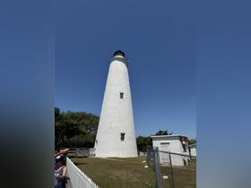 A lighthouse stands tall against a clear blue sky, with visitors nearby, capturing a scenic moment at this coastal landmark.